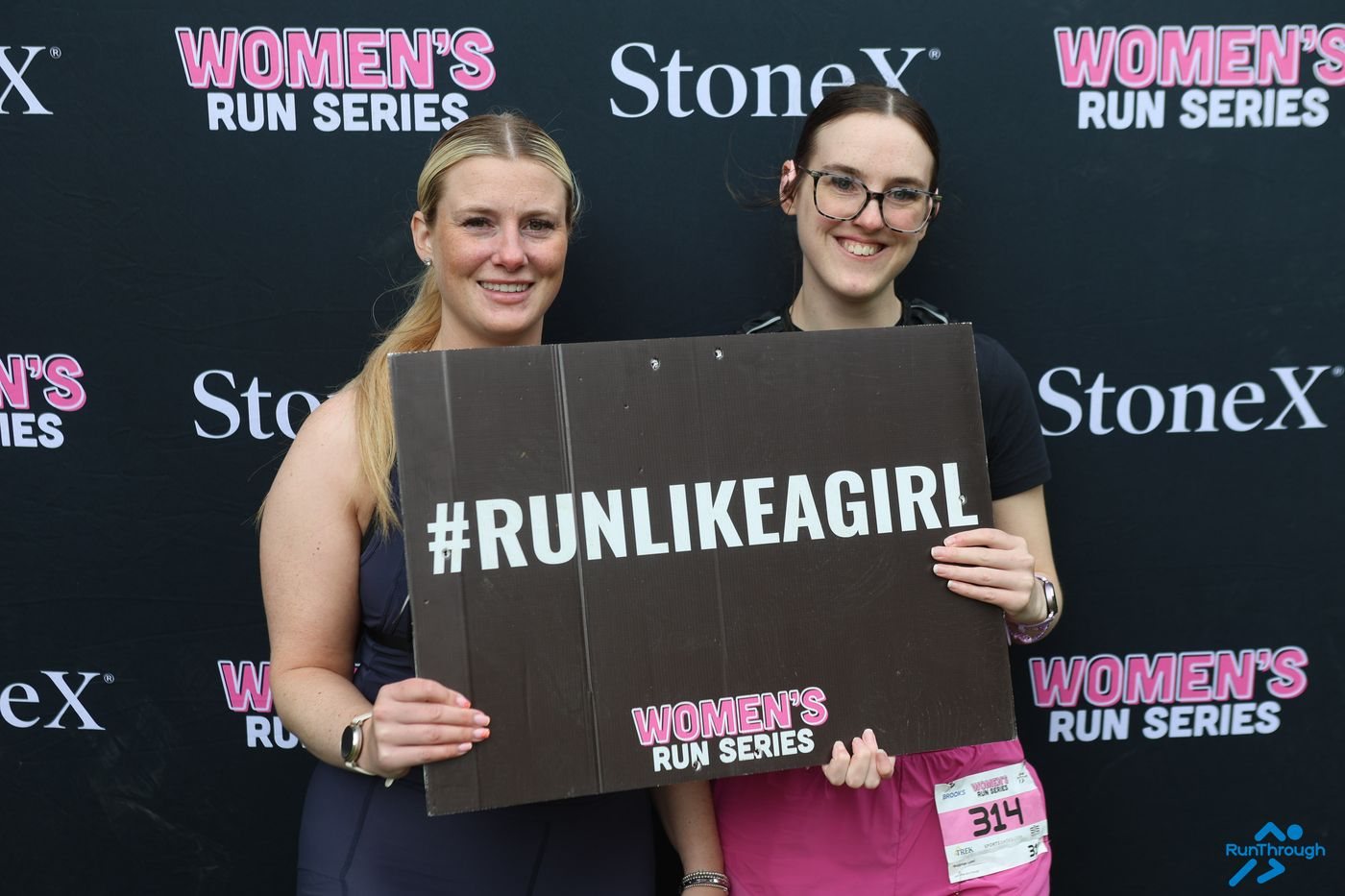 Two runners holding a #RunLikeAGirl sign at the Women's Run Series backdrop